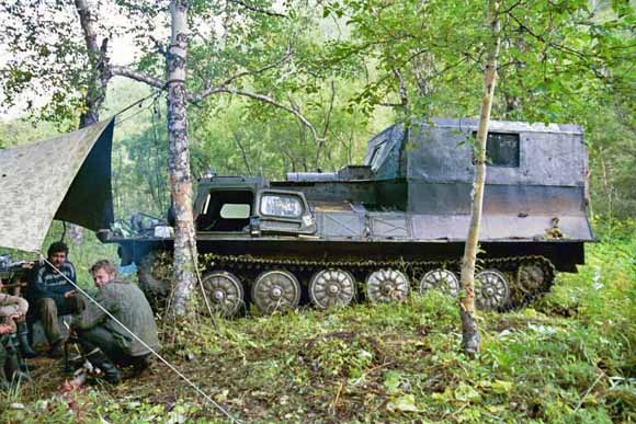 photo of field workers in foreground and Army-looking vehicle in background