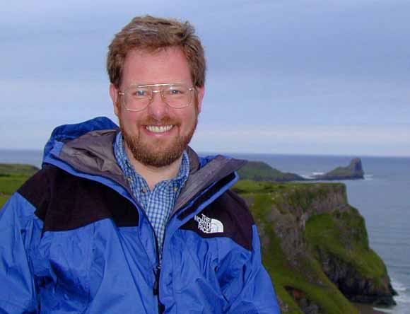 photo of Simon with a rocky coastline behind him